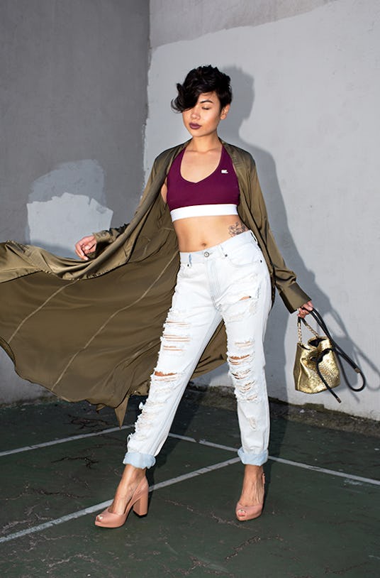 Lynn Kim wearing light ripped jeans, a burgundy top, and an olive jacket while holding a black and g...