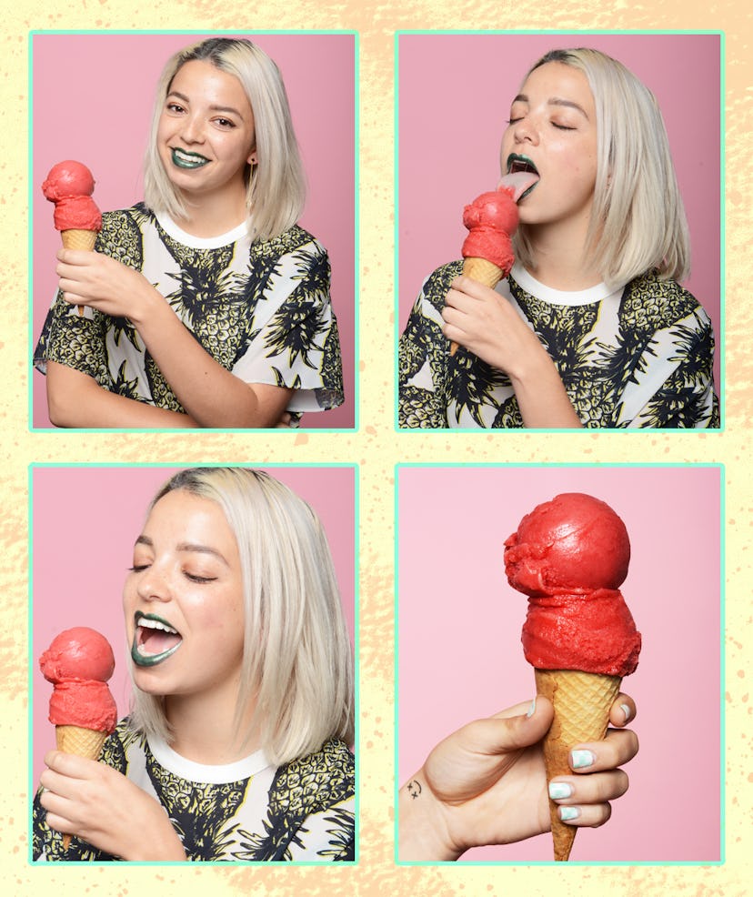 A woman with blonde hair and green lipstick eating a red ice cream cone