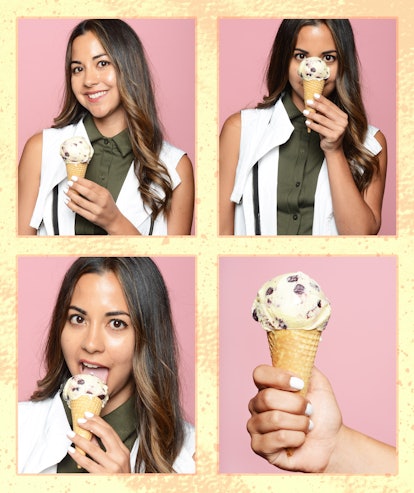 A brunette woman in a white and olive shirt eating an ice cream cone