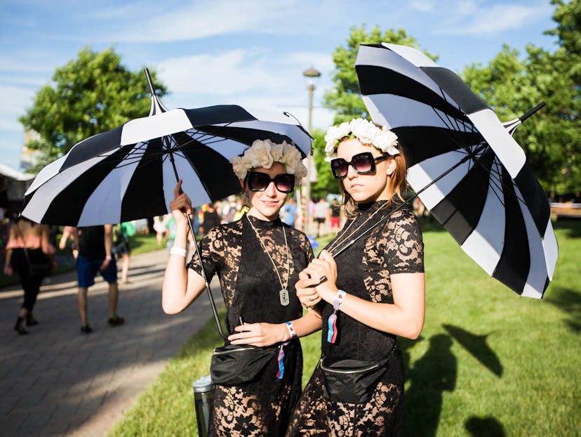 Two girls dressed in black lace dresses with white flower crowns on their heads and square sunglasse...
