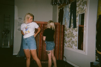 Two women checking themselves in a mirror, looking at the vintage cutoff shorts they're both wearing