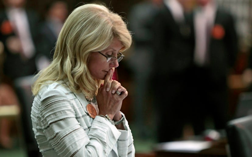 Wendy Davis wearing a white striped blazer, a pearl necklace, and glasses while looking down pensive...