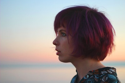 A side profile view of Jazz Morley wearing a black floral shirt in front of a blue-pink sky in the b...