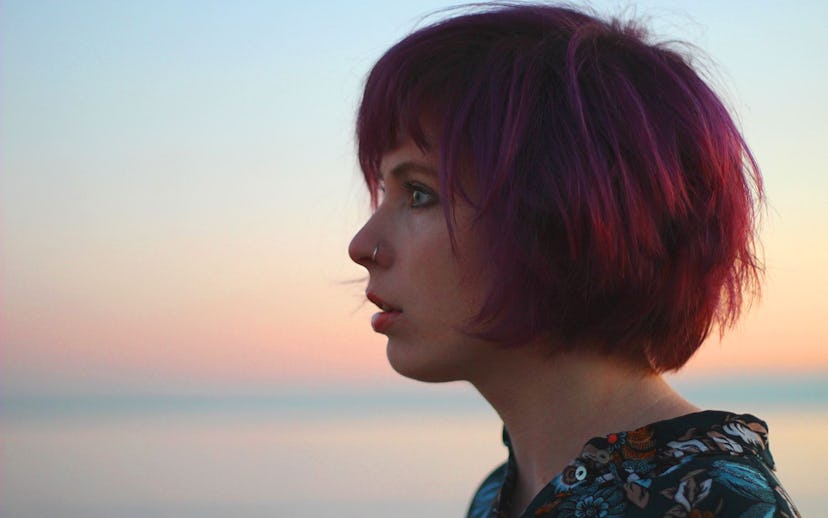 A side profile view of Jazz Morley wearing a black floral shirt in front of a blue-pink sky in the b...