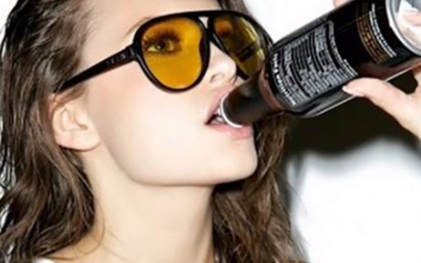 Woman in "babes and beers" shirt and yellow sunglasses drinking a bottle of beer