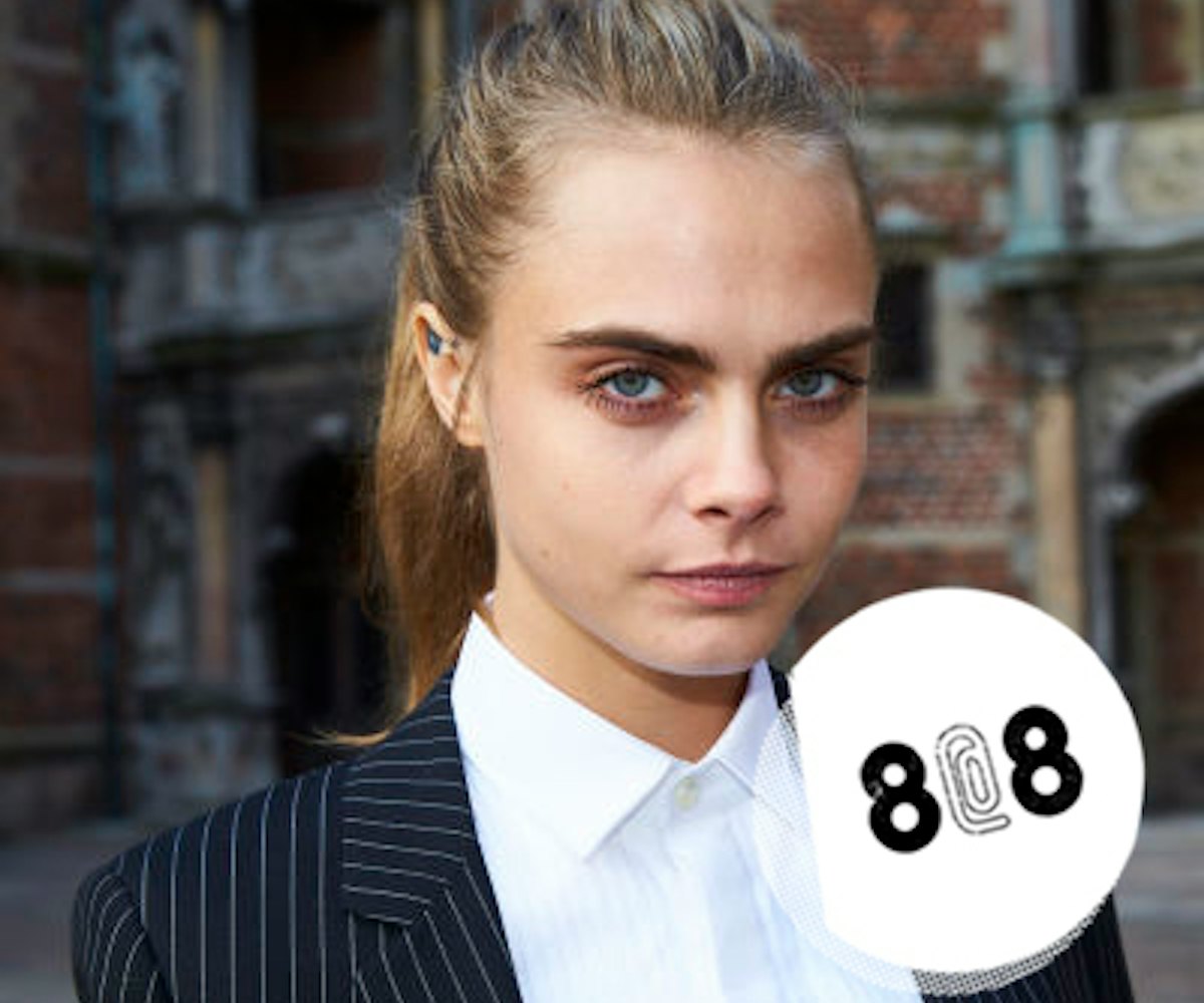 Cara Delevingne posing in a white button-up and black striped blazer 