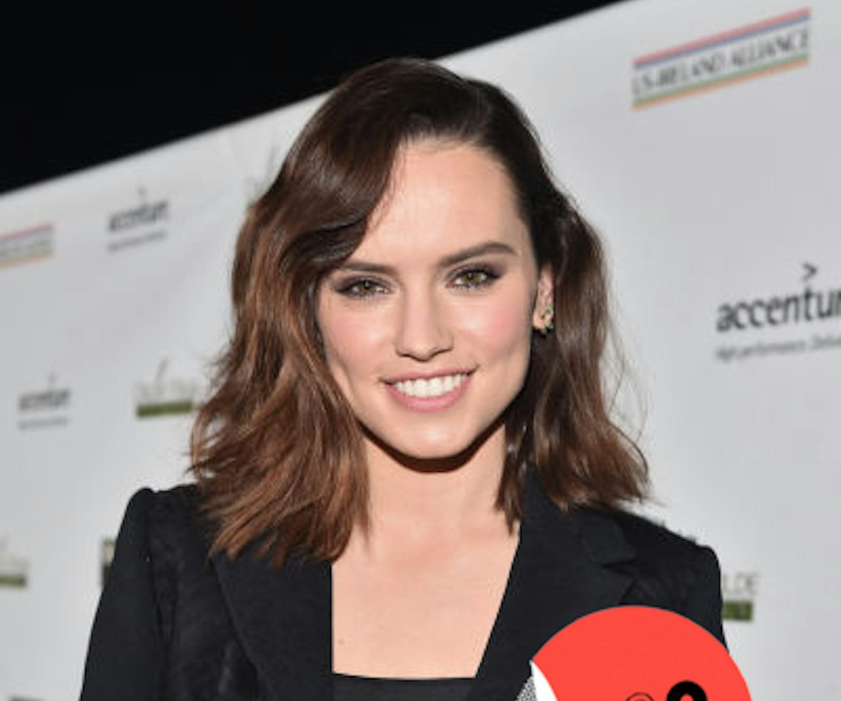 Daisy Ridley with brown wavy hair posing in a black suit