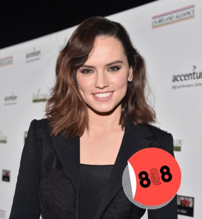 Daisy Ridley with brown wavy hair posing in a black suit