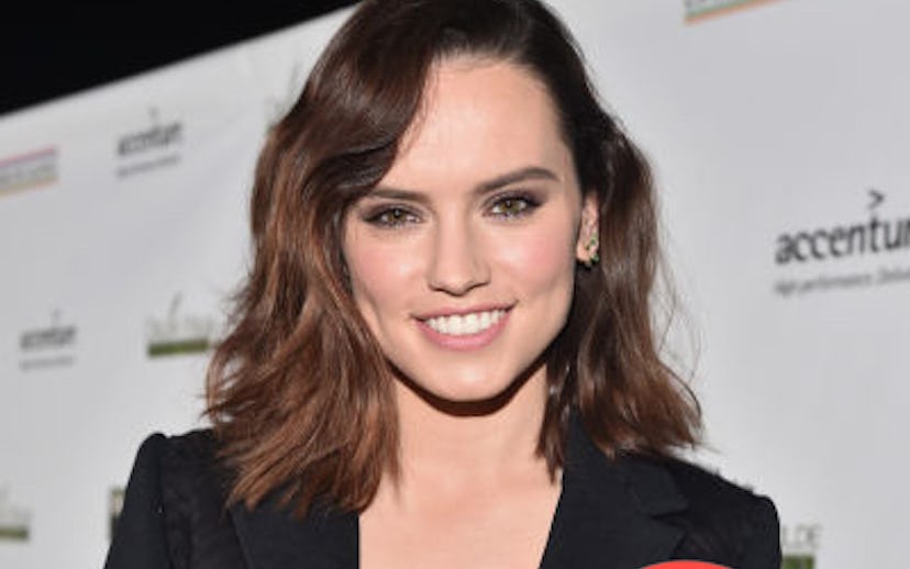 Daisy Ridley with brown wavy hair posing in a black suit