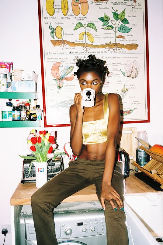 Leomie Anderson sitting on top of a washing machine, drinking coffee 