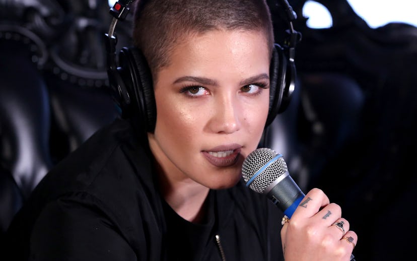 Halsey in a black bomber jacket and dark makeup holding a microphone