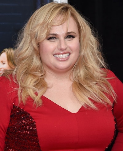 Rebel Wilson in a red dress with shiny details talking about being singe and female-driven comedies.