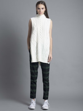 Brown-haired woman wearing a white Cable Knit Vest Dress, checkered black and green trousers, and wh...