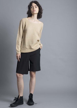 A woman with black hair wearing a Lioness - Camel Oversized Knit, black shorts, and black sneakers