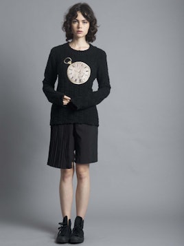 A black-haired woman wearing black shorts, a Seven & Seven sweater from the AGAIN Collection, and bl...