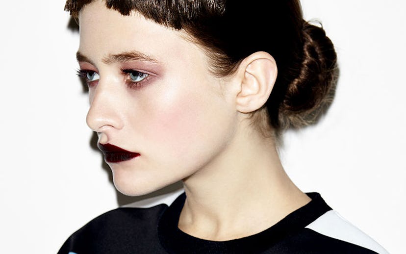 A model with dark hair and short bangs wearing simple eye make-up and black lipstick