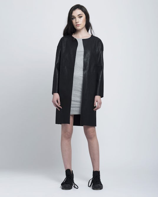 A model posing in Blackblessed's long vegan leather jacket, a grey dress and black sneakers 