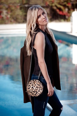 Nicky Hilton posing while wearing a black shirt and black pants and holding a brown coat