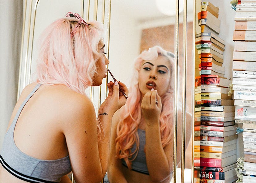 Model with pink hair wearing pink Crap Eyewear sunglasses on her head while doing her makeup