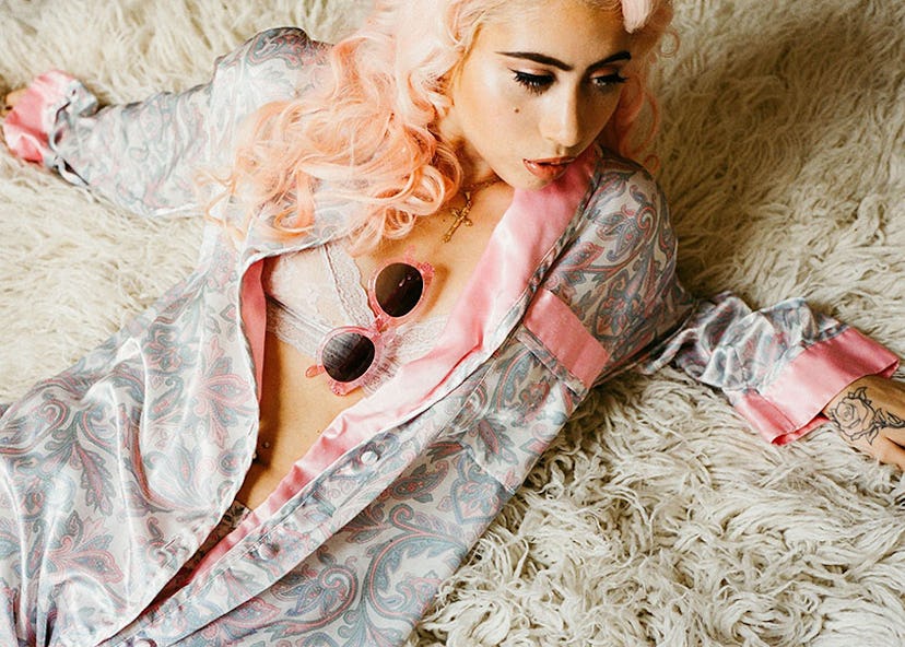 Model with pink hair lying on a rug with pink Crap Eyewear sunglasses tucked in her bralette 
