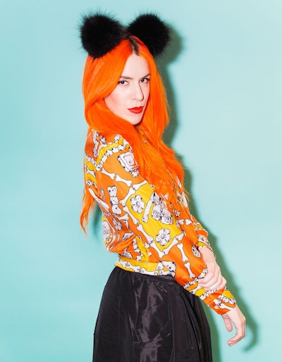 Kerin Rose Gold with bright orange hair with two black pom-poms in an orange shirt with a bone-like ...