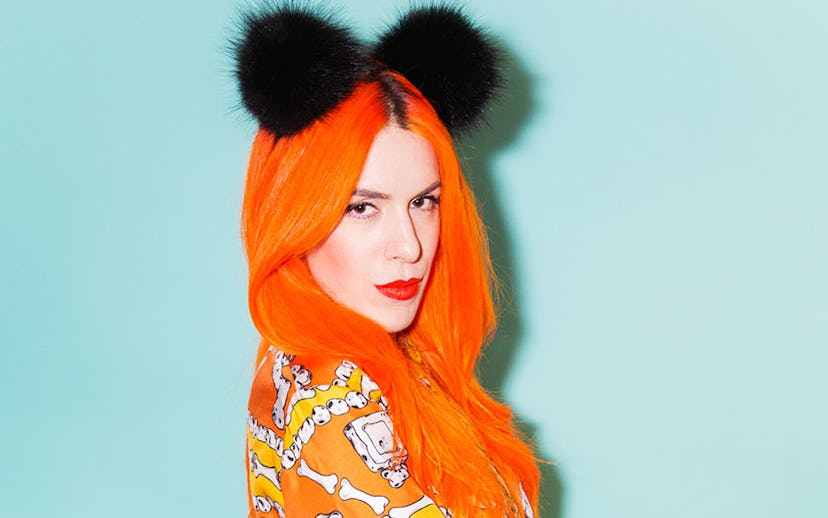 Kerin Rose Gold with bright orange hair with two black pom-poms in an orange shirt with a bone-like ...
