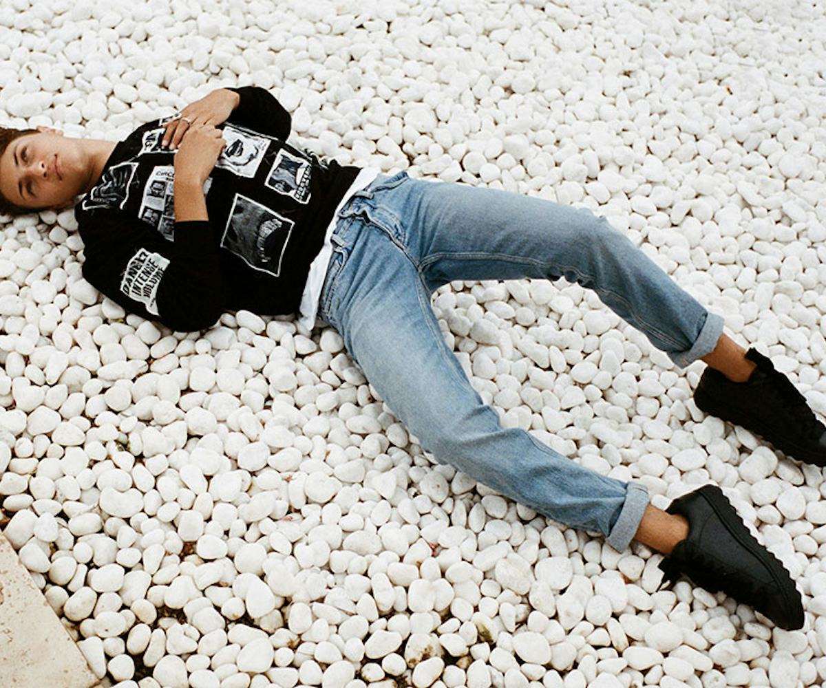 Anwar Hadid wearing a black shirt and jeans while lying on rocks