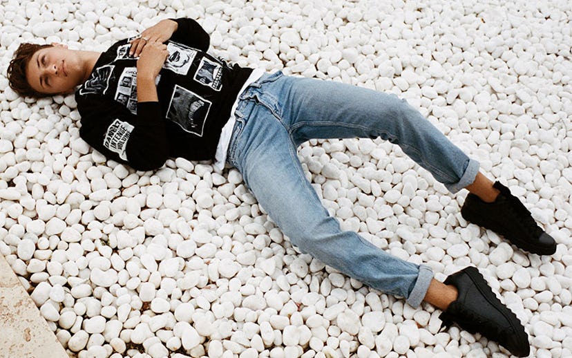 Anwar Hadid wearing a black shirt and jeans while lying on rocks