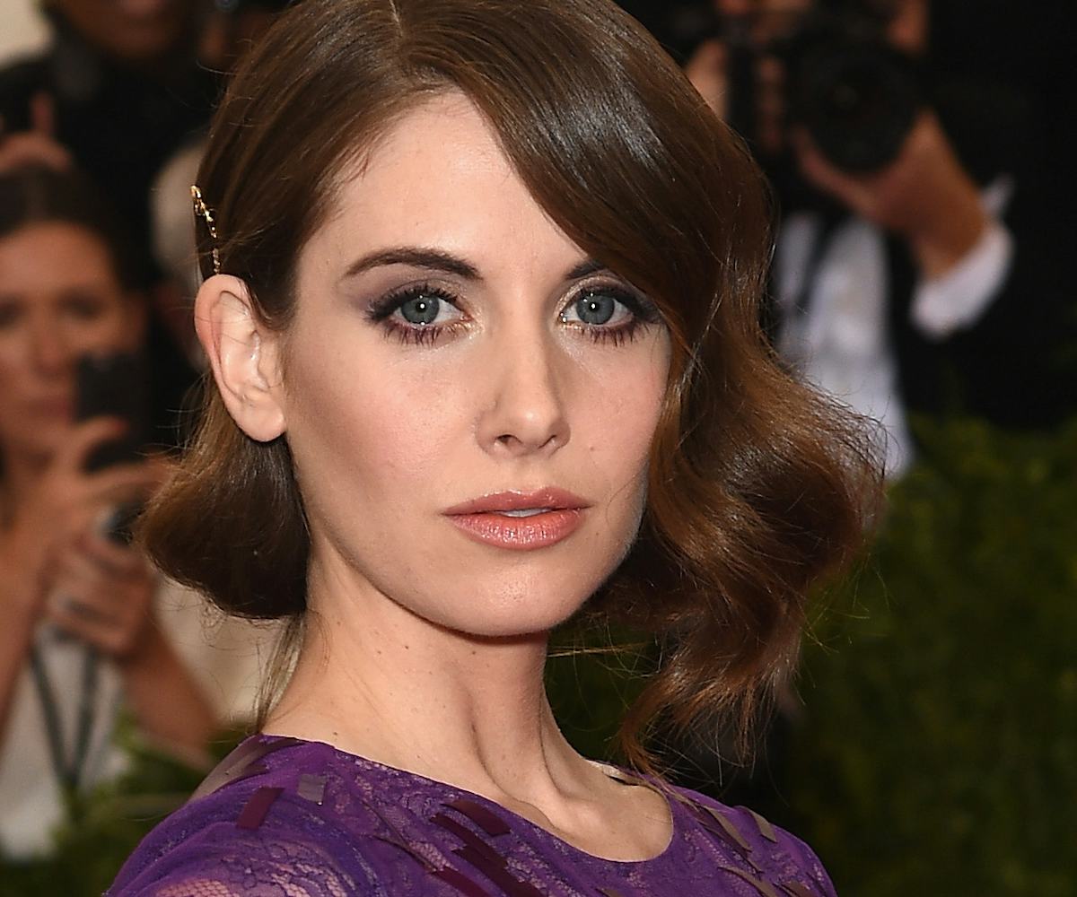 Alison Brie in a purple dress on the red carpet with paparazzi behind her