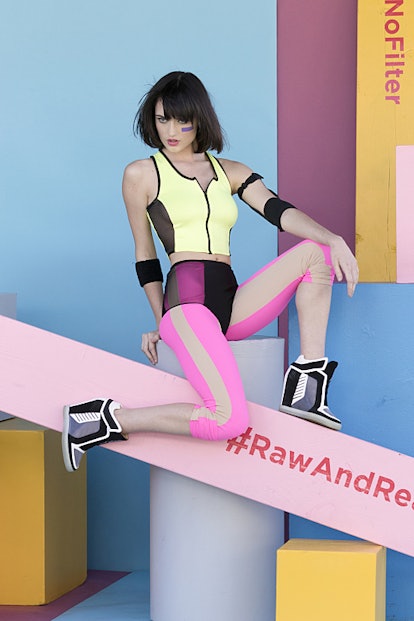 A female model in a colorful combination posing on a wooden shape with "#RawandReal" text