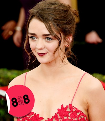 Maisie Williams in a red dress with her hair in a bun.