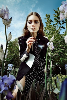 Model playing with flowers in a black jacket by Carven and black dress by Frame Denim