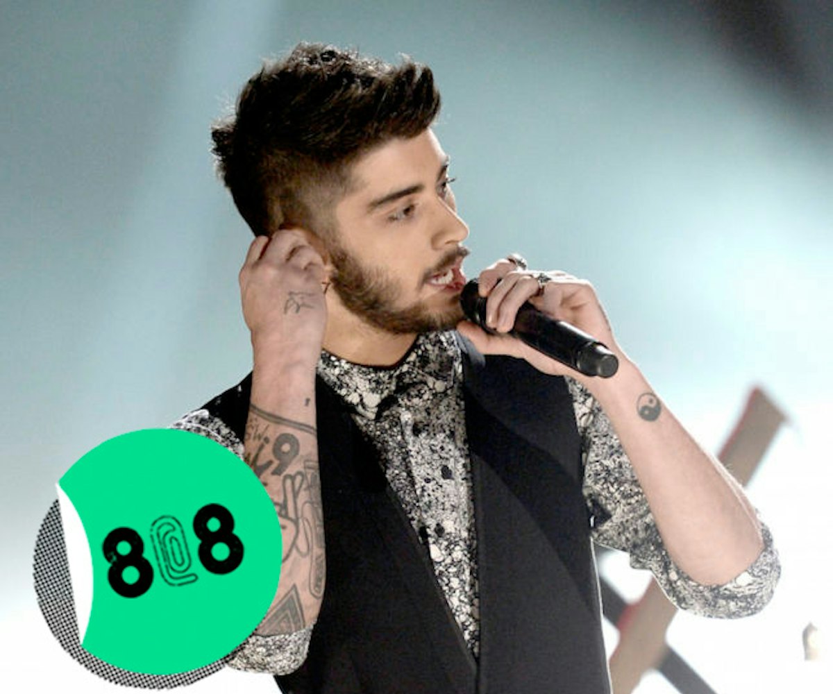 Zayn Malik in a black and shirt and a black vest hand performing on stage holding a microphone and s...
