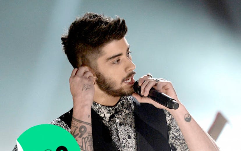 Zayn Malik singing while wearing a black and white shirt and a black vest hand