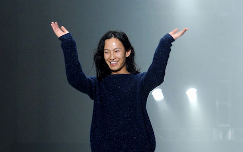 Alexander Wang on the runway in a navy blue sweater with his hands in the air