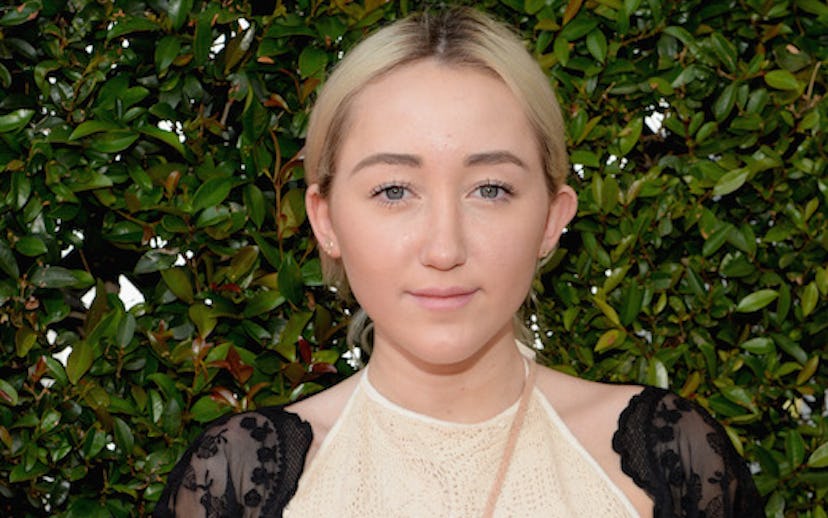 Noah Cyrus posing in front of a green bush