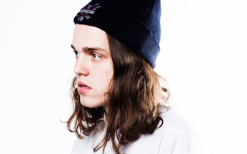 A male model posing in a white shirt and a black beanie with mid length brown wavy hair