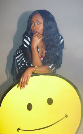 Tink in a black and white striped and polka dot dress, posing with a large smiley face cutout 