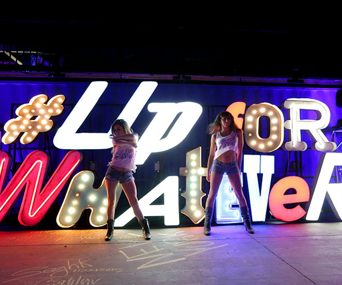 Two girls dancing with the glowing sign reading "Up for whatever" in the background at the EDM event