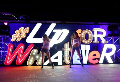 Two girls dancing with the glowing sign reading "Up for whatever" in the background at the EDM event