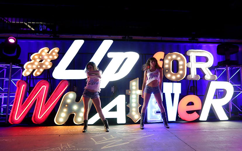 Two girls dancing with the glowing sign with "Up for whatever" text in the background at the EDM eve...