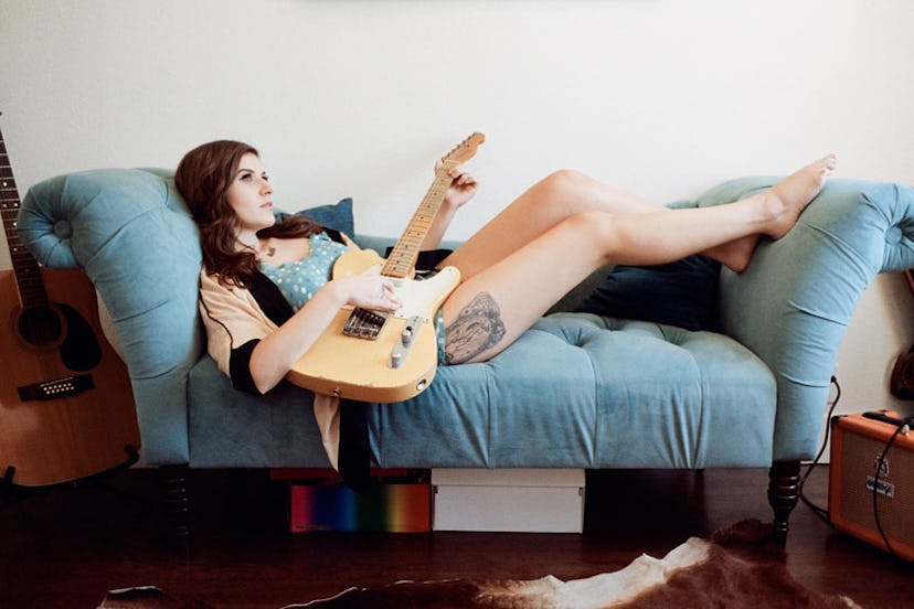 Bethany Cosentino lying on a sofa while holding a guitar