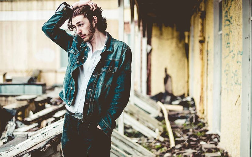 Hozier pushing back his hair and looking to the side while wearing a white shirt, denim jeans, and a...