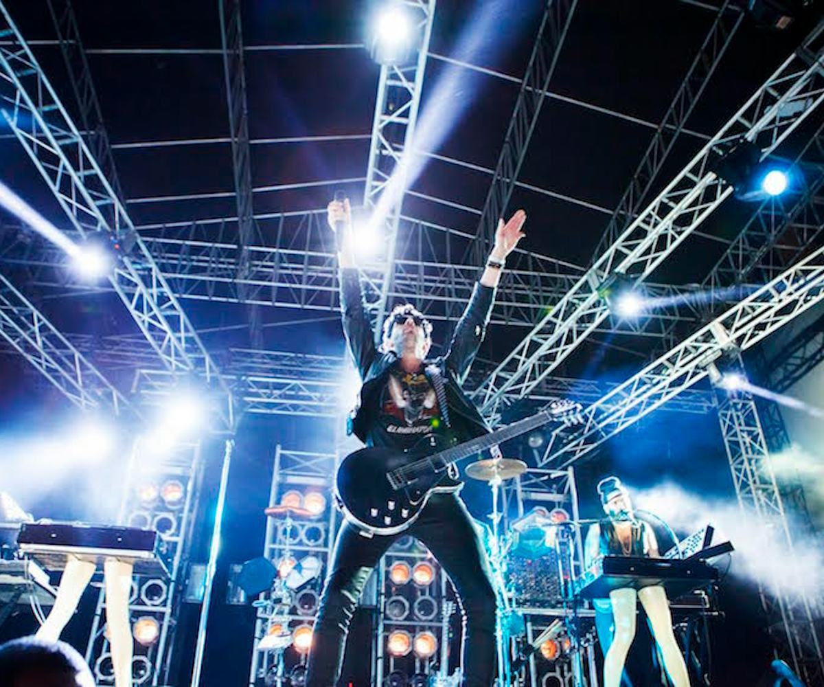 A rock band mid-performance, with their bass player having his hands up in the air