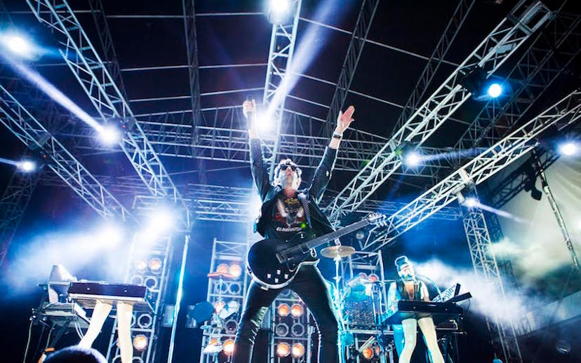 A rock band mid-performance, with their bass player having his hands up in the air