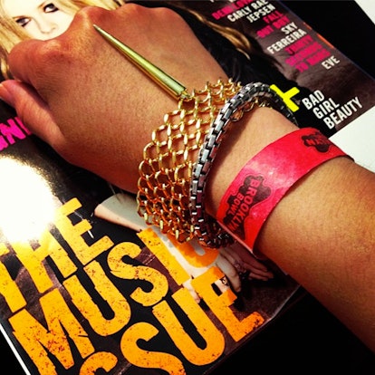 A hand with golden chain bracelets and a red festival ticket wristband