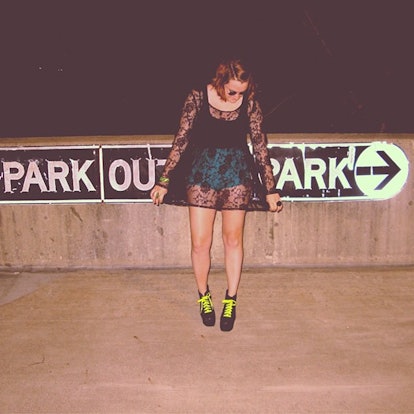 A girl wearing a black tank top, green shorts and a sheer black long shirt while posing for a photo