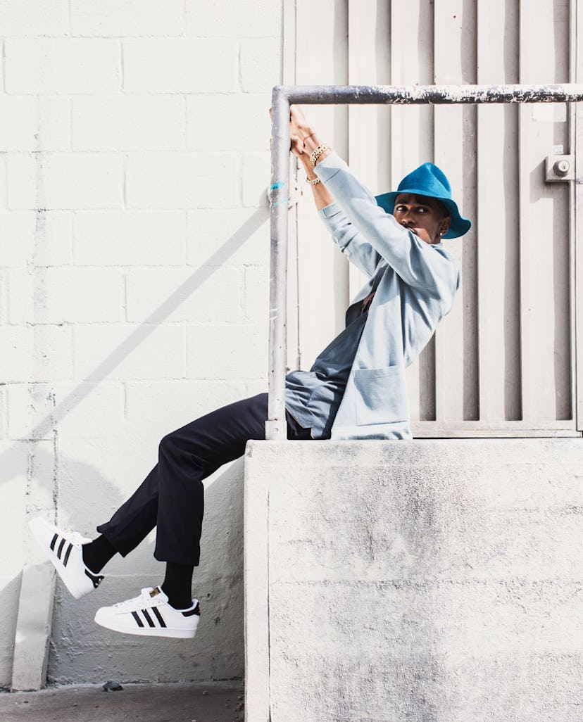 Big Sean in a light blue jacket and a blue fedora hat while holding onto a railing with his feet in ...