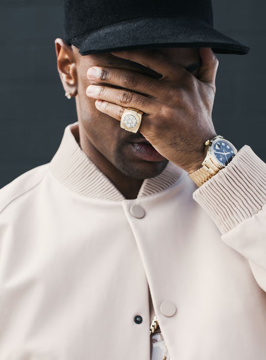 Big Sean in a white jacket and a black hat, covering his face with his hand