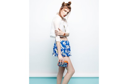 A model wearing an Ukulele anika sheer white top, Love Sadie floral shorts, and a Etre ikat clutch